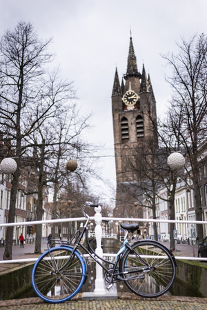 Delft, Netherlands - January 6 2019: The leaning tower of the old church in Delft. In front a bike leaning against the railing of a bridge over the canal Oude Delftの写真素材