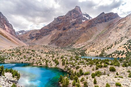The beautiful mountain trekking road with clear blue sky and rocky hills and the view of Alaudin lake in Fann mountains in Tajikistanの写真素材
