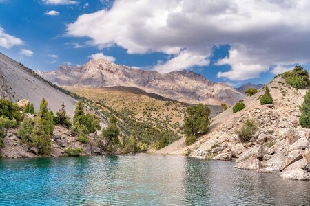 The beautiful mountain trekking road with clear blue sky and rocky hills and the view of Alaudin lake in Fann mountains in Tajikistanの写真素材