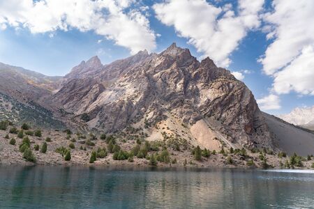 The beautiful mountain trekking road with clear blue sky and rocky hills and the view of Alaudin lake in Fann mountains in Tajikistanの写真素材