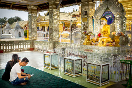 Mandalay/Myanmar-05.03.2017:Man and woman sitting and playing mobile phone in front of Buddha statue