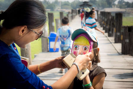 Taungthaman/Myanmar-05.03.2017:Mother putting on her daughter a mask from the russian cartoon Masha...