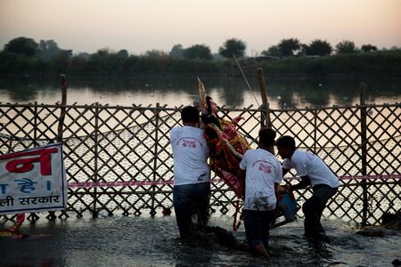 New Delhi / India â September 30 2017: Three unidentified men submerging an idol of Hindu goddess Durga on the occasion of Durga Visarjan on the Yamuna River in New Delhi.のeditorial素材