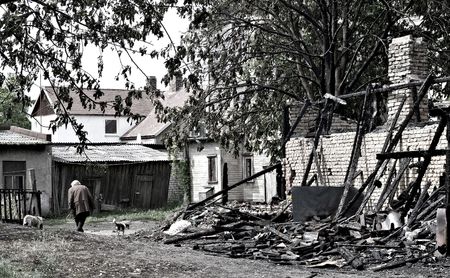 Poor woman with two dogs walking near a burnt houseの写真素材