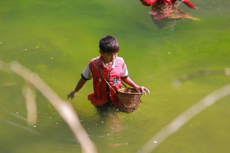 Bandarban, Bangladesh-December 15,2018: Angry little aboriginal boy catching fish into river in traditional way.のeditorial素材