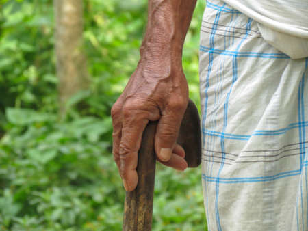 An old Indian man standing by holding wooden walking stick in the village of Bangladesh.の写真素材