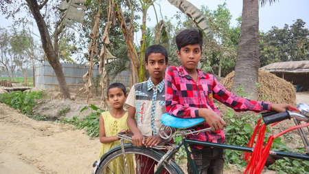 Rajshahi, Bangladesh-March 8,2021:Two boys and a girl of village standing on the street with their old bicycleのeditorial素材