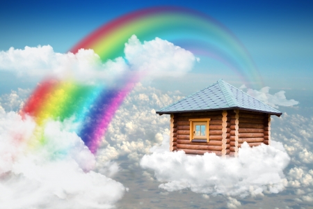 Small wooden house flying on cloud in sky near rainbowの写真素材