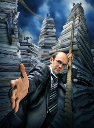 Serious businessman inviting you to climbing up the pile of paperworkの写真素材