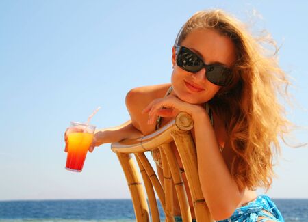 Beautiful young girl in glasses with cocktail on the beachの写真素材