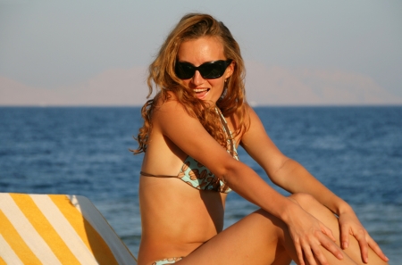 Young woman in glasses on chaiselongue with sea on backgroundの写真素材