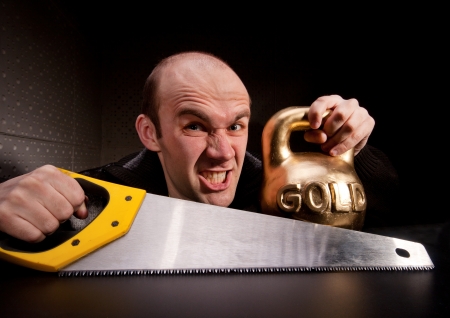 Crazy man with saw and heavy weight of goldの写真素材