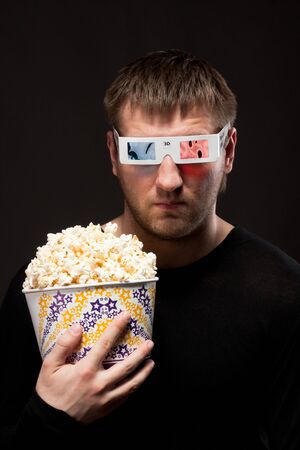 Portrait of serious man watching 3D movie and holding bucket of popcornの写真素材