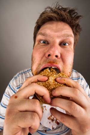 Portrait of expressive fat man chewing hamburgerの写真素材