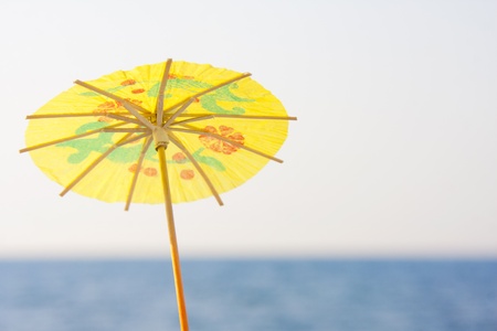 Yellow cocktail umbrella by the seaの写真素材