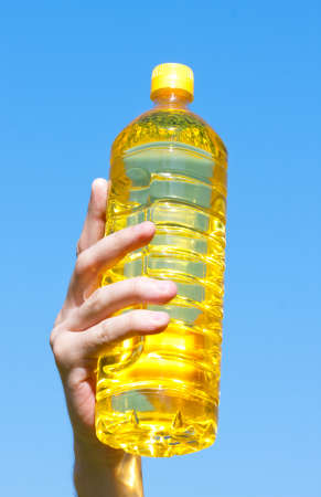 Hand holding bottle of sunflower oil against clear blue skyの写真素材
