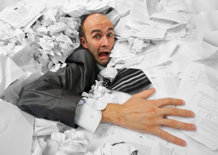 Businessman sinking in heap of documents and asking for helpの写真素材