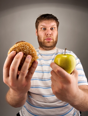 Portrait of man choosing between hamburger and green appleの写真素材