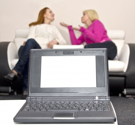 Laptop with blank screen and two talking woman on backgroundの写真素材