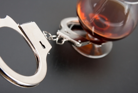 Close-up of handcuffs lock with glass of alcohol on backgroundの写真素材