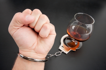 A hand locked to glass of alcohol by handcuffsの写真素材