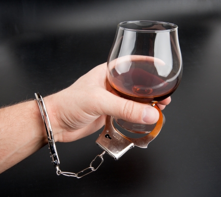 A hand locked to glass of alcohol by handcuffsの写真素材