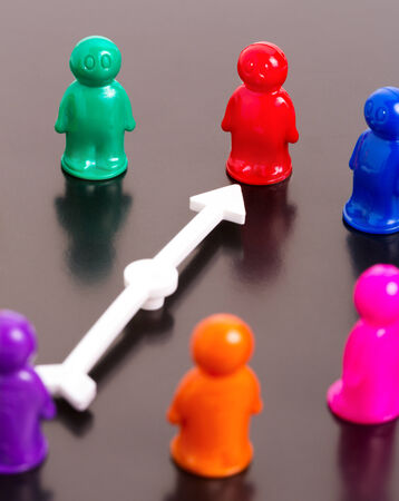 Group of toy people and white arrow pointing on the red oneの写真素材