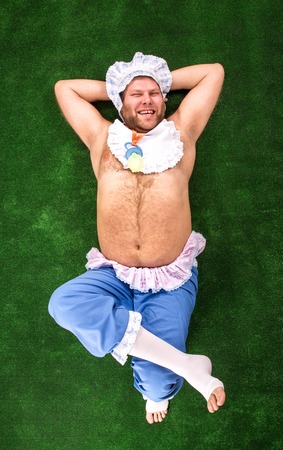 Man weared as baby having rest on grassの写真素材