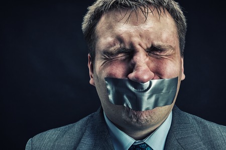 Man with mouth covered by masking tape preventing speech, isolated on blackの写真素材