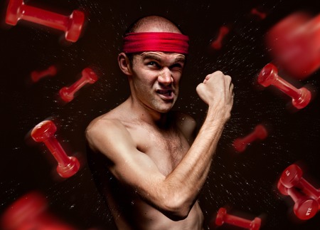 Funny geek shows his muscles with flying dumbbells aroundの写真素材