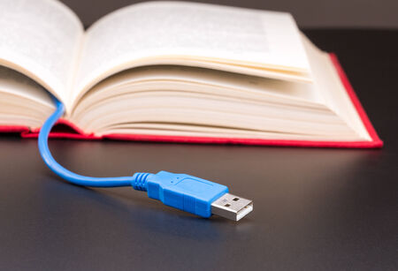 Blue usb cable sticks out from red bookの写真素材