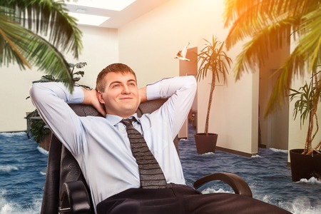 Businessman is dreaming about vacations in his officeの写真素材