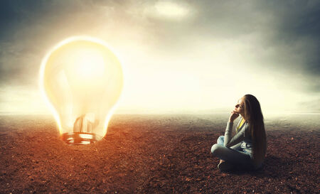 Woman sitting on a ground and looking at big lamp, idea conceptの写真素材