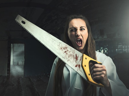Scary portrait of an angry crazy woman with a bloody saw in her handの写真素材
