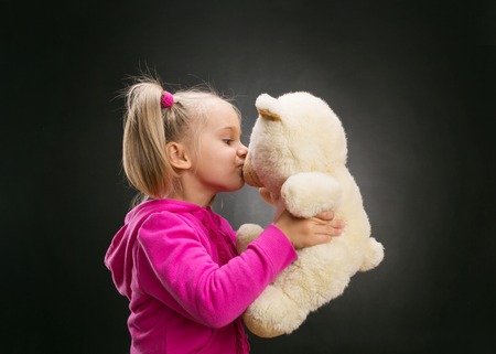 Little cute girl kisses toy bear on greyの写真素材