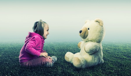 Small cute girl sits and looks at toy bear on white and green backgroundの写真素材