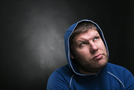 Adult man in the hood sits thinking on dark background