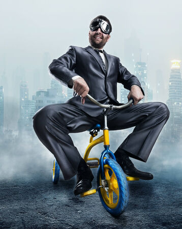 Odd businessman riding a small bicycle against dark city backgroundの写真素材