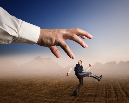 Businessman runs in a desert from a big arm