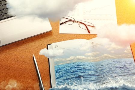Office table in clouds with the sea on the notebookの写真素材
