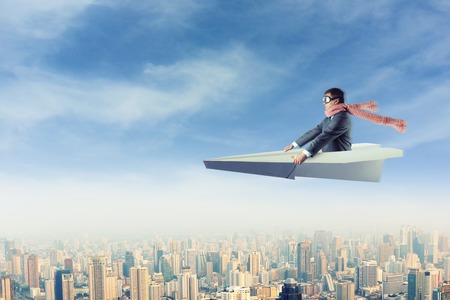 Businessman with the scarf on paper airplane above the cityの写真素材