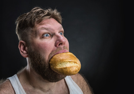 Side view of a man eating a big bread over blackの写真素材