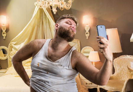 Glamour ugly man with beard takes selfie in bedroomの写真素材