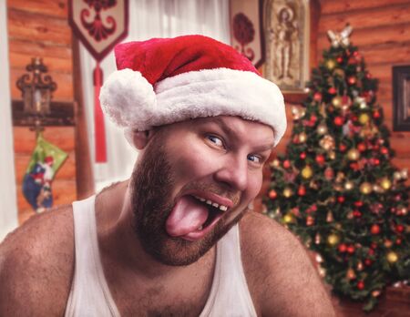 Smiling man in Santa Claus hat showing his tongue at homeの写真素材