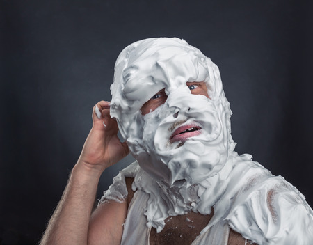 Crazy man with face completely in shaving foam thinks over greyの写真素材