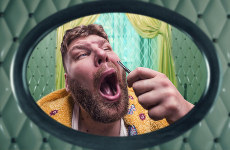 Strange adult man pulls out filament from his nose looking in the mirrorの写真素材