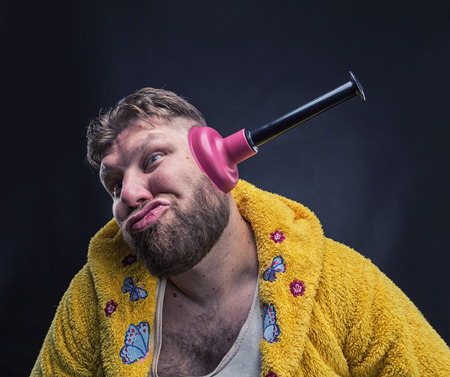 Strange man in a terry bathrobe with a plunger in his earの写真素材