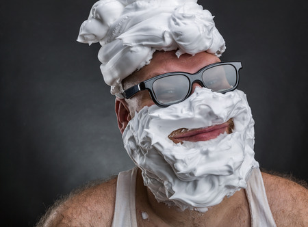 Strange smiling man in glasses with shaving foam on his face and on his head closeupの写真素材