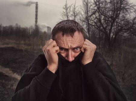 Scared man hides his face in sweater on natureの写真素材