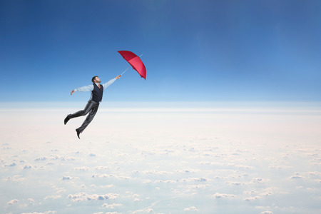 Man flying in the sky with red umbrella in his handの写真素材
